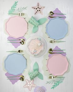 there is a cake on the plate with mermaid decorations around it and other items in pastel colors