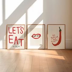 three framed art pieces on the floor in front of a white wall with words that read let's eat