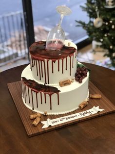 a three tiered cake with chocolate drizzle and wine glass on top is sitting on a wooden table