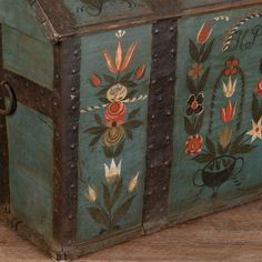 an old wooden trunk with painted flowers and leaves on the sides, sitting on a wood floor