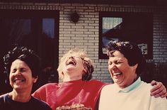 three people laughing and standing in front of a brick building