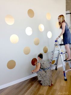 a woman is painting a wall with gold polka dot decals on it and a man in a ladder