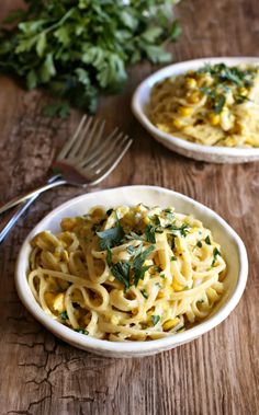 two white bowls filled with pasta and garnished with parsley next to a fork