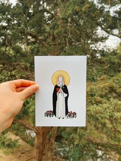 a person holding up a card with an image of the virgin mary in front of trees