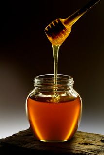 honey being poured into a glass jar with a wooden spoon in it on top of a piece of wood