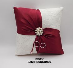 a red and white pillow with a ring bearer on it's side that is tied to the back of another pillow