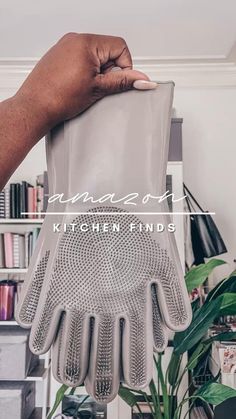 a person holding up a kitchen strainer in front of a potted plant and bookshelf