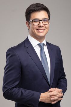 a man in a suit and tie posing for the camera with his hands folded up