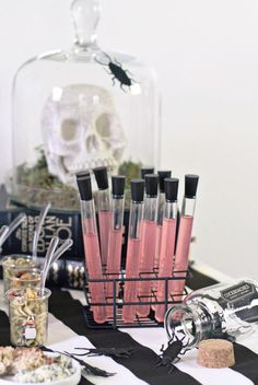 a table topped with lots of bottles filled with pink liquid next to a skeleton head