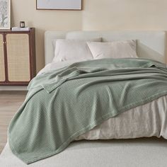 a bed with a green blanket on top of it next to a dresser and lamp