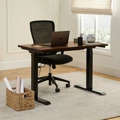 a desk with a laptop on it and a basket next to it in front of a window