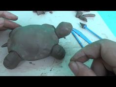 two hands are working with clay to make a small turtle sculpture on the table next to some pencils