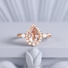 a pink diamond ring sitting on top of a white table next to a pair of pearls