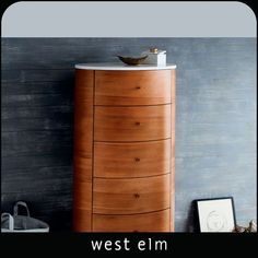 a tall wooden cabinet sitting next to a gray wall with a white bowl on top