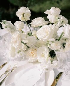 white flowers are in vases on a table with silverware and napkins around it