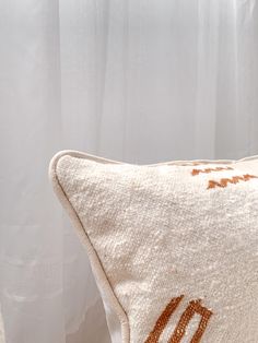 a white pillow with an orange design on the front and back, sitting next to a window