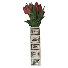 a white vase with red flowers in it on a white background, that is decorated with black and white geometric designs