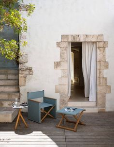 two chairs and a table sitting on a wooden deck next to an open window with white drapes