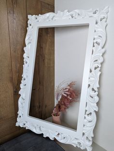 a white framed mirror sitting on top of a wooden floor next to a vase filled with flowers