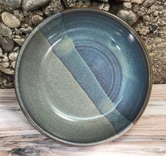 a blue and green plate sitting on top of a wooden table next to some rocks