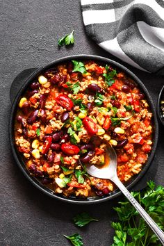 a skillet filled with beans and rice on top of a table next to some parsley