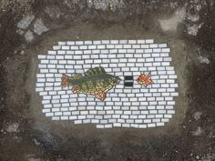 two fish painted on the ground next to a brick wall with white and black tiles