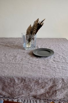 a table topped with a glass vase filled with dried grass next to a plate on top of a bed