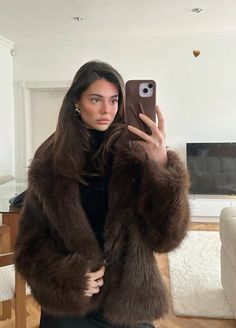 a woman is taking a selfie with her cell phone while wearing a fur coat