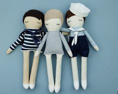 three dolls are laying next to each other on a blue surface, one is wearing a sailor's hat and the other has eyes closed