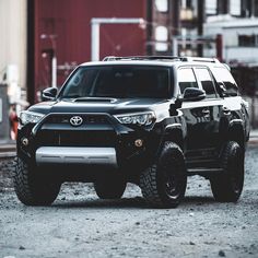 a black suv parked on the side of a train track next to a red building