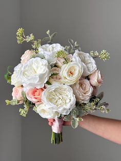 a bridal bouquet being held by someone's hand in front of a gray wall