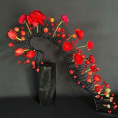 a black vase with red flowers in it next to a wire sculpture on a table