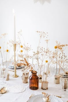 a white table topped with lots of plates and vases filled with flowers next to a candle