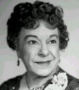 an old photo of a woman with curly hair and flowers on her collar smiling at the camera