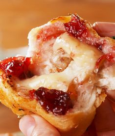 someone is holding up a pastry with cranberry sauce and cheese on it's crust