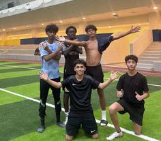 four young men posing for a photo on a soccer field with their hands in the air