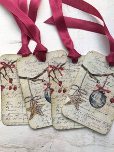 four tags with red ribbons hanging from them on a white wooden surface, decorated with writing and ornaments