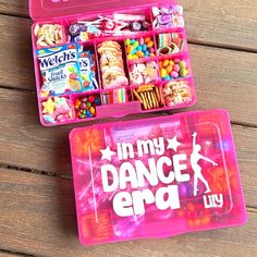 two pink lunchboxs filled with candy and snacks on top of a wooden table