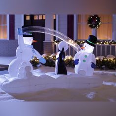 two snowmen in front of a house with christmas lights on the windows and trees behind them