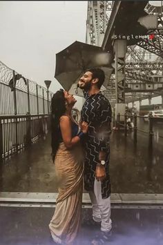 a man and woman standing under an umbrella on a rainy day in front of a bridge