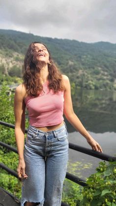 a woman standing on top of a metal rail next to a body of water with trees in the background