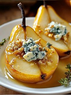 two pears with blue cheese and herbs on top are sitting on a white plate