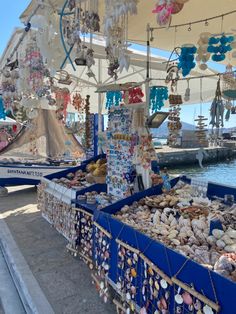 an outdoor market with various items for sale on the water and boats in the background