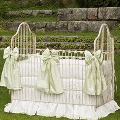 a white crib with green bows on it in the grass next to some rocks