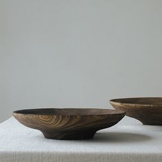 two wooden bowls sitting next to each other on a tablecloth covered surface with white walls in the background