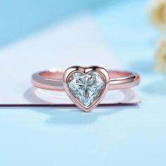 a heart shaped diamond ring on top of a blue surface with flowers in the background