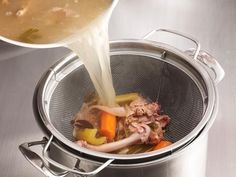 someone pouring soup into a pot with vegetables