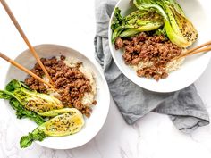 two bowls filled with meat and vegetables on top of a white tablecloth next to chopsticks