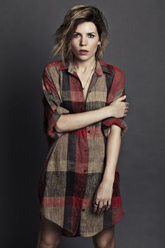 a woman standing with her arms crossed and looking at the camera, wearing a plaid shirt dress