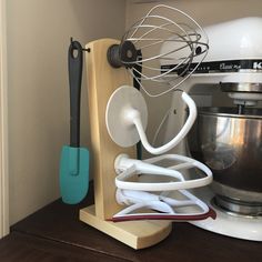 a kitchen mixer, whisk attachment and spatula holder on a wooden stand